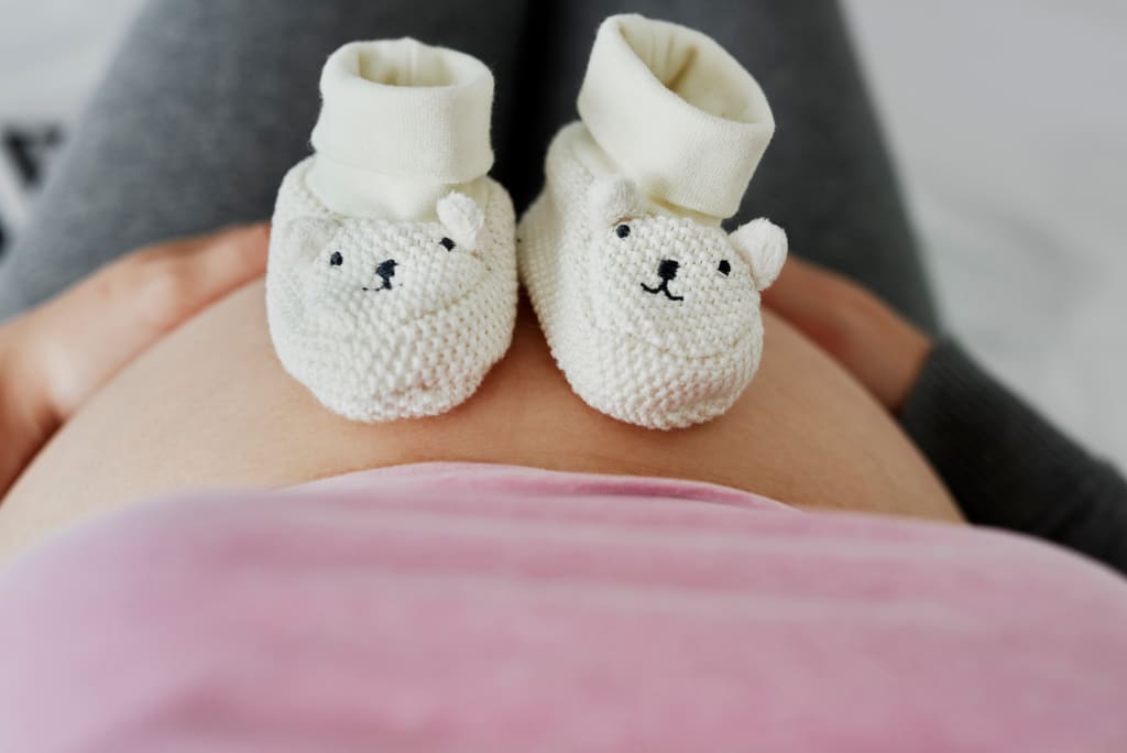 Knitted baby booties resting on a pregnant woman's belly — Pregora free pregnancy calculator hero