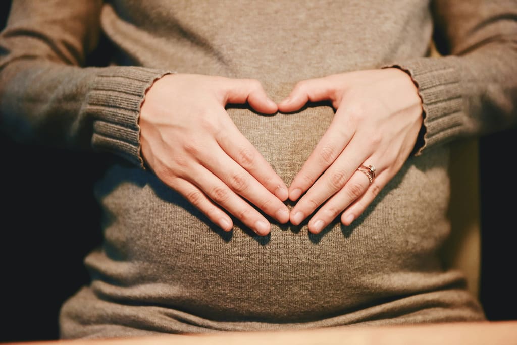 Pregnant woman forming a heart shape with her hands on her belly — trusted Pregora pregnancy calculator
